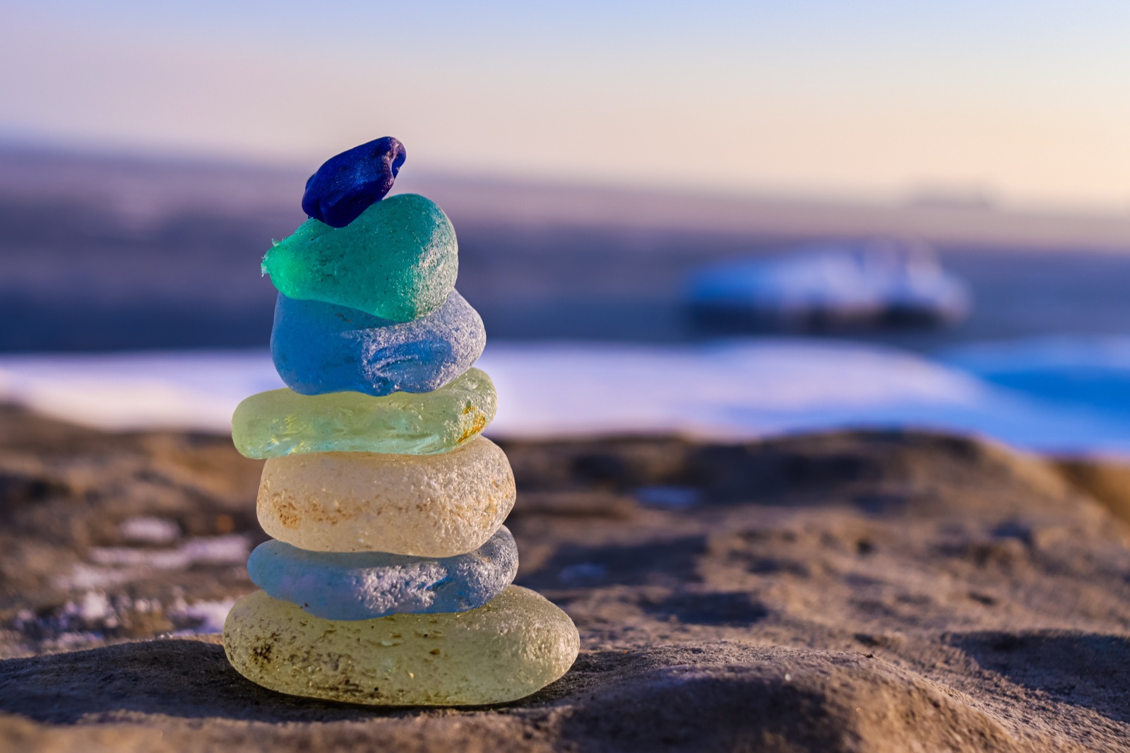 A small cairn of frosted sea glass — cobalt, teal, blue, pale green, and amber — stacked on the rocks at golden hour