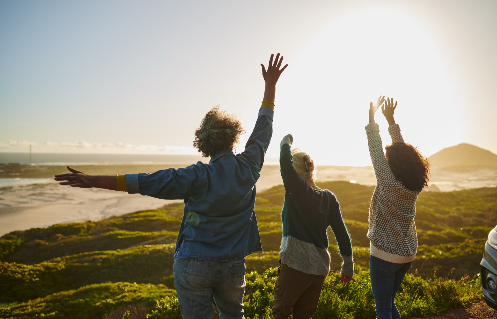 Three retreat guests with arms raised on the sunlit headland above the sea