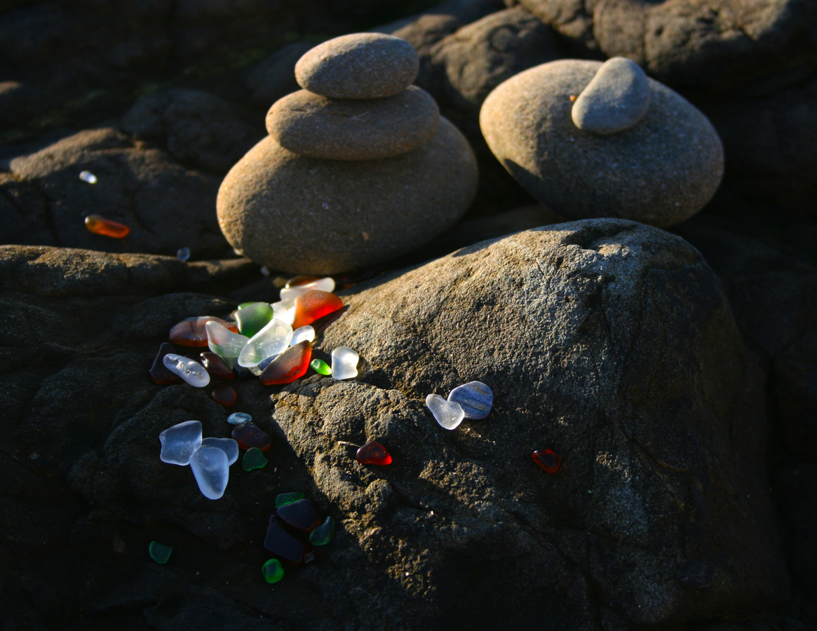 Frosted sea glass among dark stones at Glass Beach in low winter light